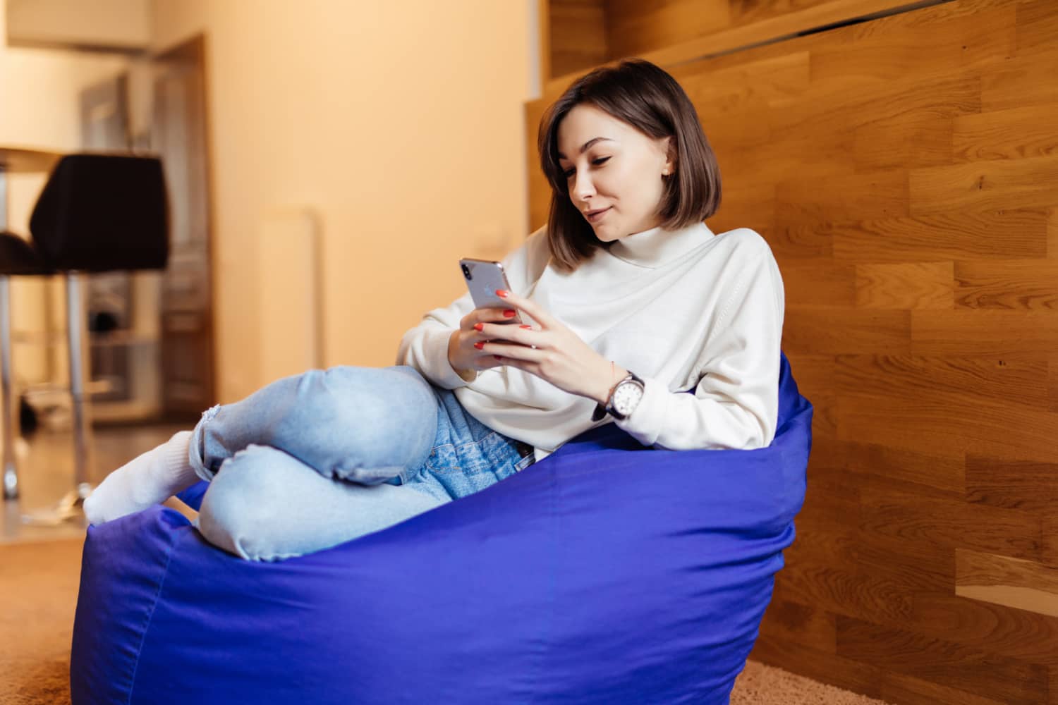 smiling woman is sitting bright violet bag chair using her phone texting with her friends